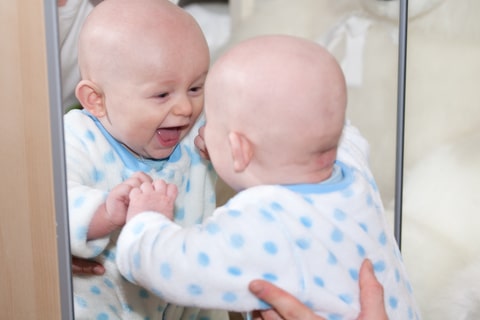 A laughing baby looking at its self similarity in the mirror