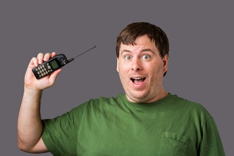 A man holding up his old cell phone from the 1990s with a pull out antenna